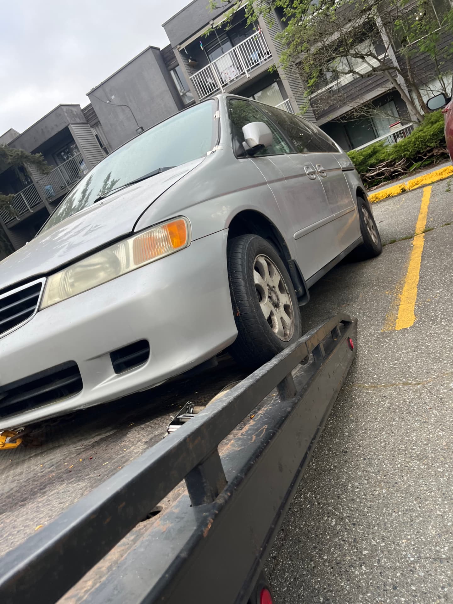 A silver Honda Odyssey minivan being winched onto Jay's flatbed in an apartment parking area